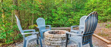 A stone fire pit surrounded by Adirondack chairs in a forested area.