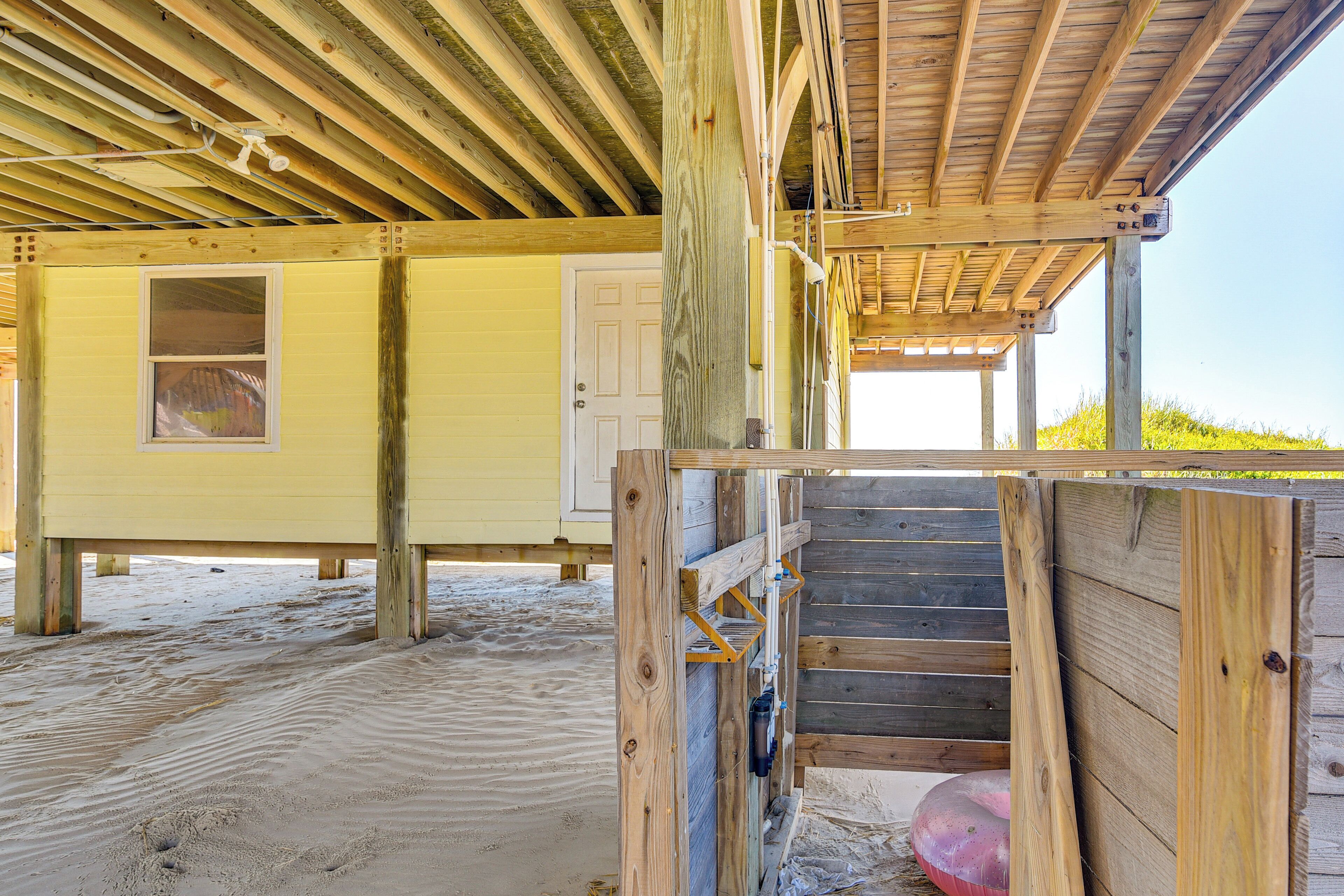 A wooden structure with a door and a window, a staircase, and a sandy ground.