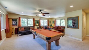A pool table in a room with a ceiling fan, large windows, and a sofa. - Groveland Vacation Rental Near Pine Mountain Lake! (Groveland)