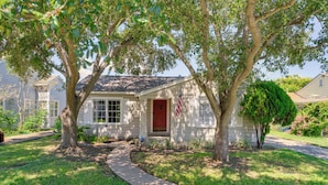 A single-story house with a red door, a front yard with a pathway, and a large tree in front. - 1939 Bungalow With Original Charm Corpus Christi (Corpus Christi)