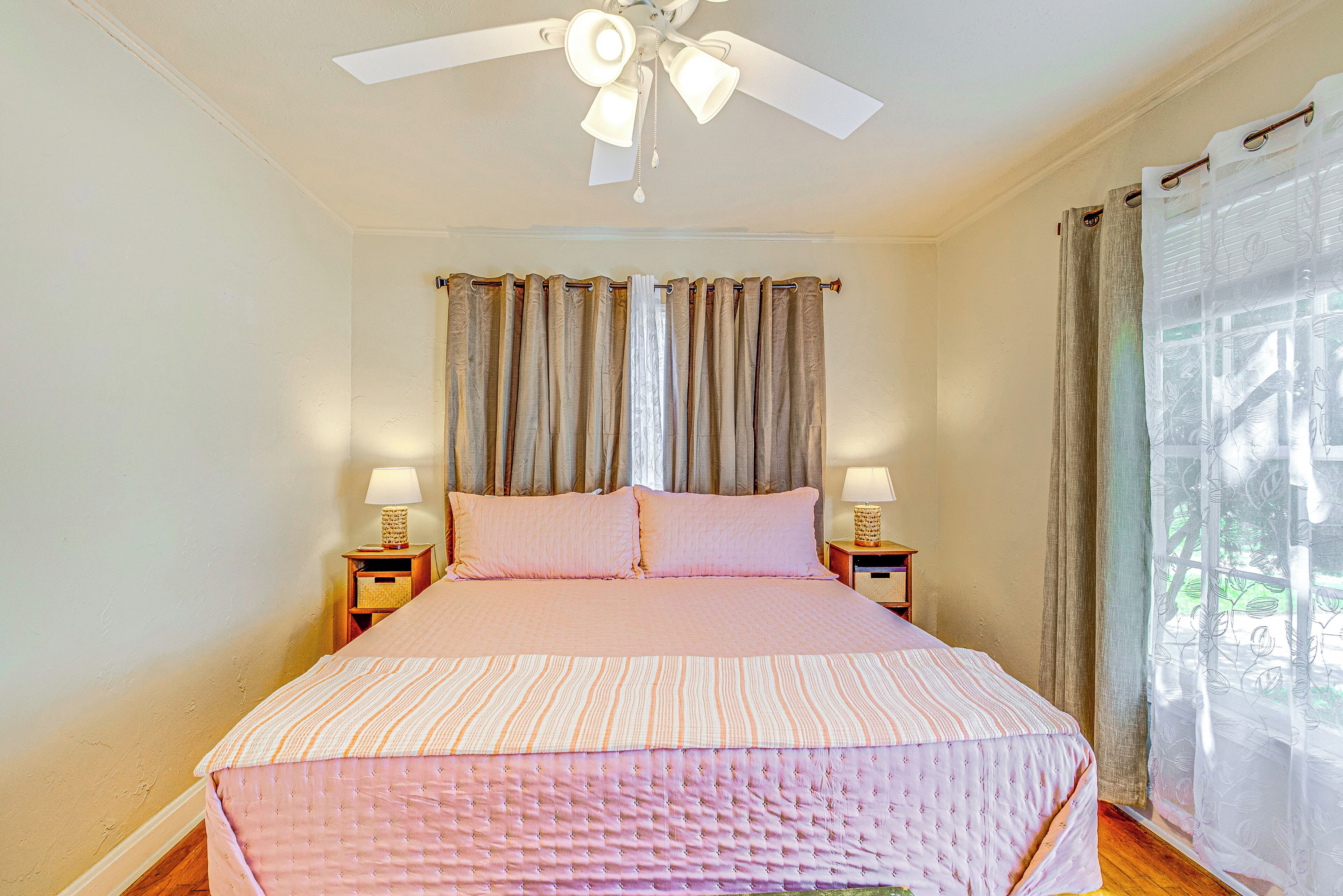 Une chambre à coucher avec un lit, deux tables de chevet, un ventilateur de plafond et des rideaux.