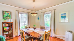 A dining room with a wooden table, chairs, and a chandelier. There are windows with curtains, a bookshelf, and a radiator. - 1939 Bungalow With Original Charm Corpus Christi (Corpus Christi)