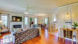 A spacious living room with a fireplace, wooden flooring, a sofa, a dining area, and a kitchen in the background. - 1939 Bungalow With Original Charm Corpus Christi (Corpus Christi)