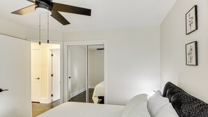 A bedroom with a bed, a ceiling fan, a door, and a hallway. - Stylish & Modern Lenexa Haven w/ Fire Pit & Deck! (Lenexa)