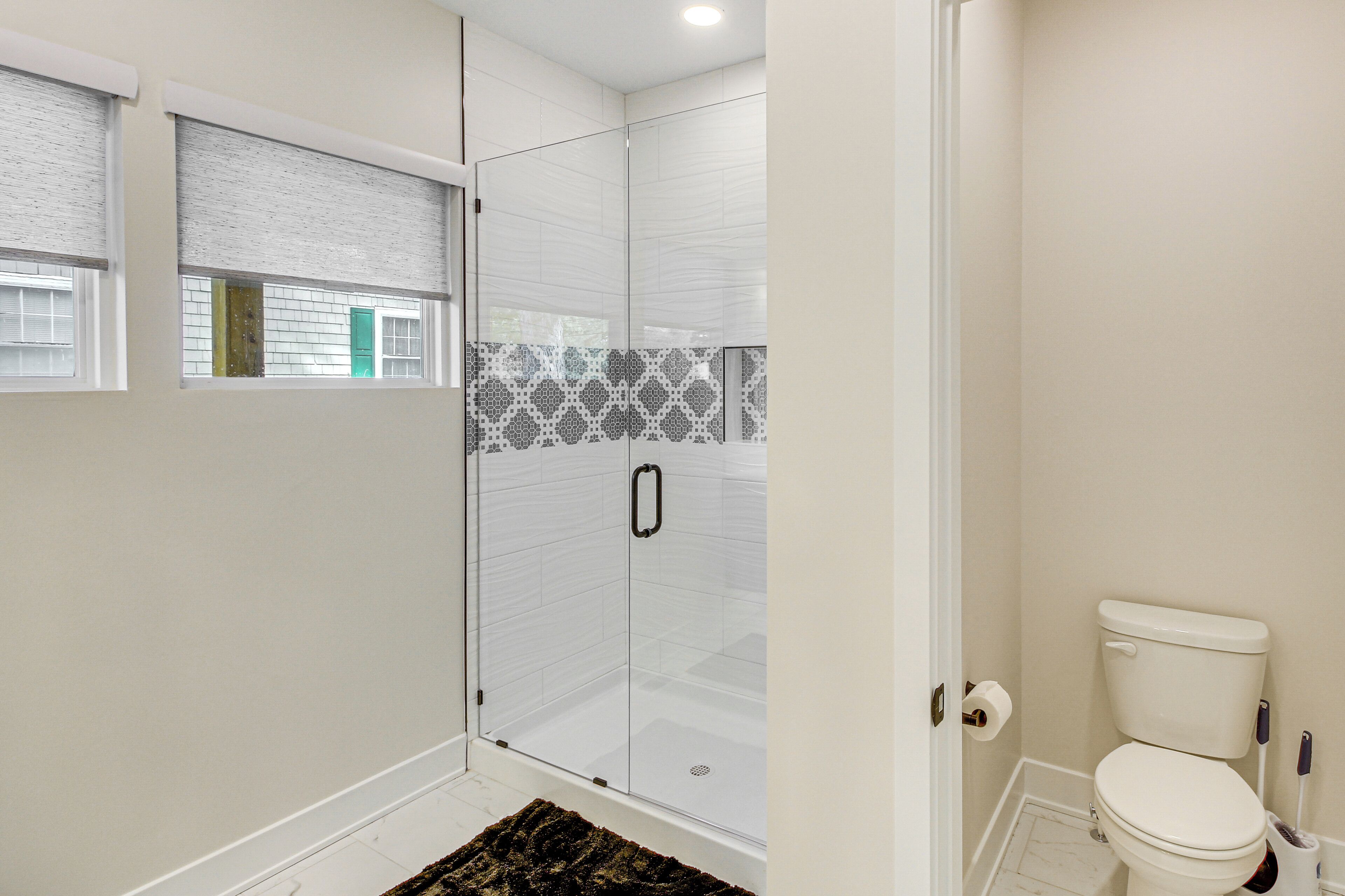A bathroom with a glass shower enclosure, a toilet, and a patterned tile backsplash.