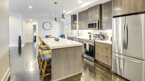 A modern kitchen with a central island, stainless steel appliances, and wooden cabinetry. - Stylish & Modern Lenexa Haven w/ Fire Pit & Deck! (Lenexa)