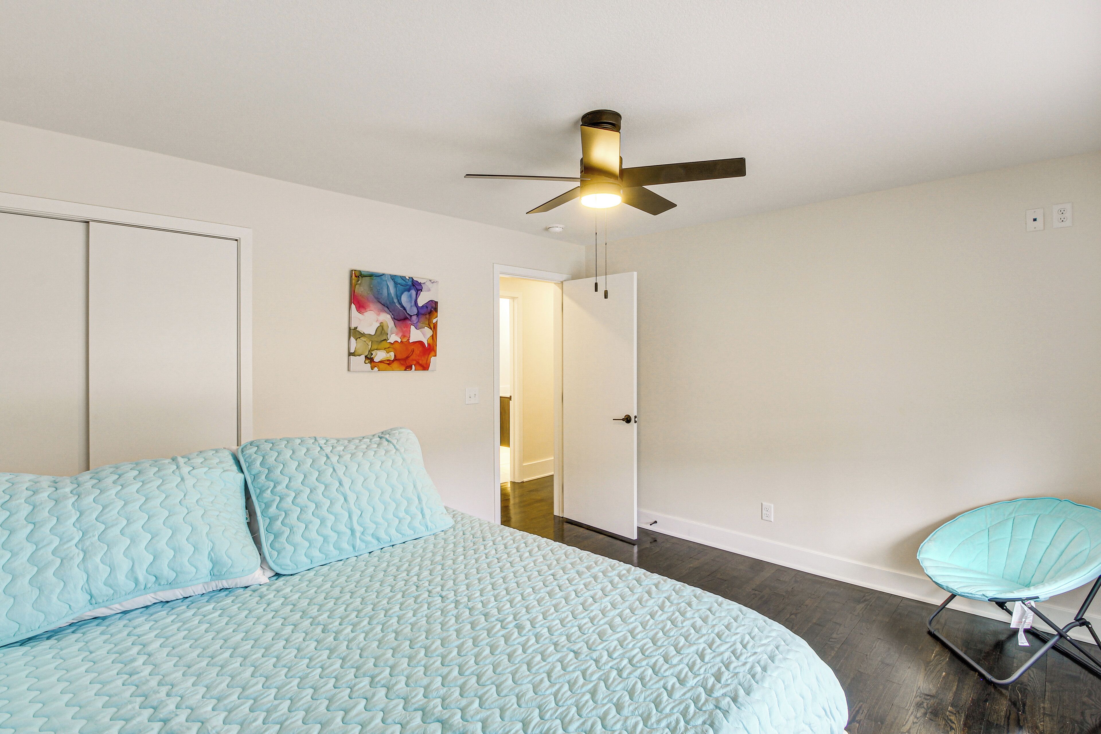 A bedroom with a bed, a ceiling fan, a door, and a chair.