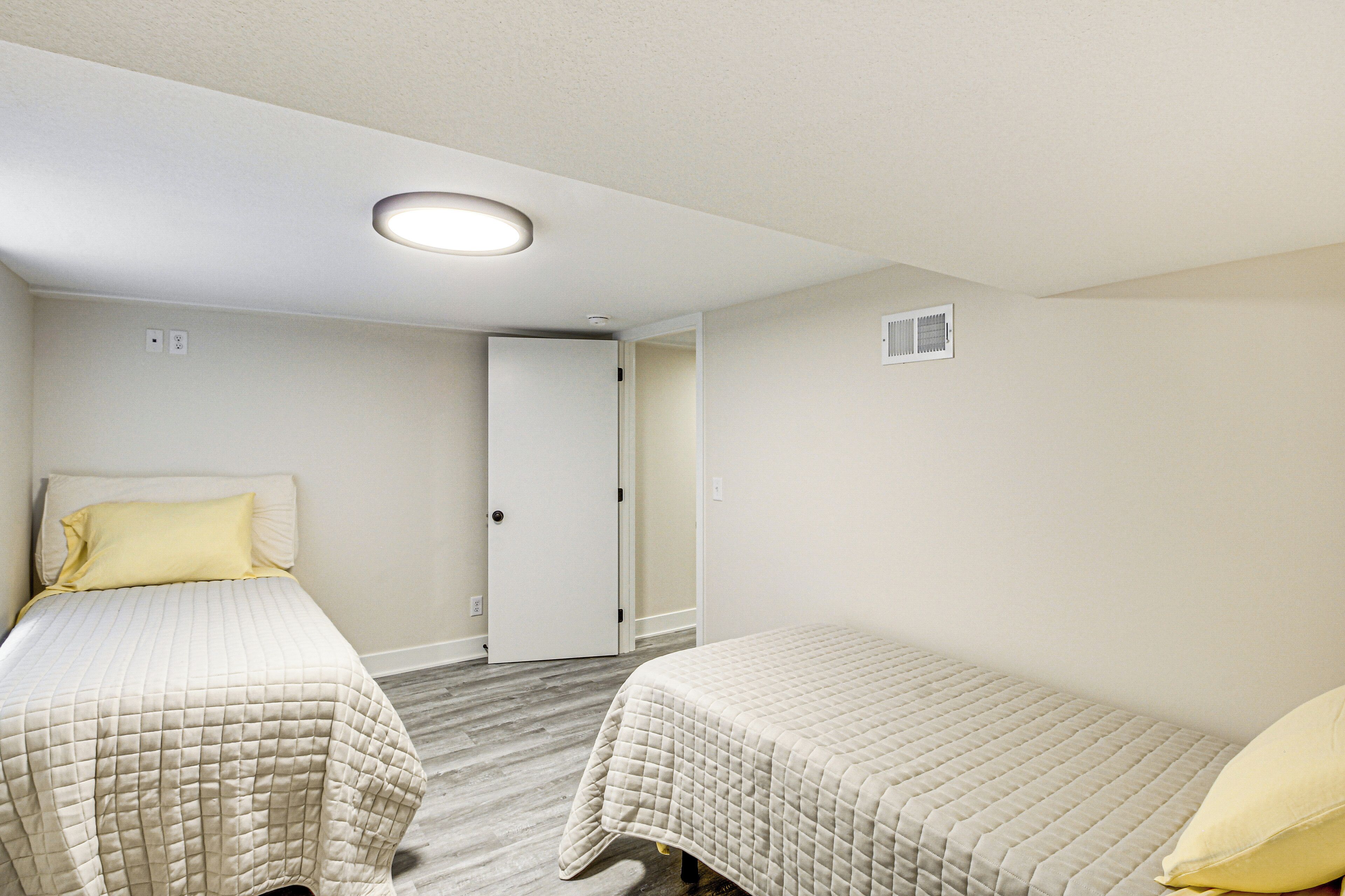A bedroom with two beds, a door, and a ceiling light.
