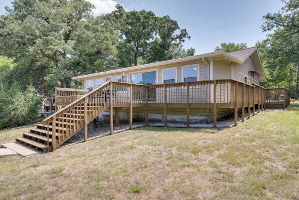 A two-story house with a wooden deck and a staircase leading to the upper level. - Lakefront College Station Home Near Texas A & M! (College Station)