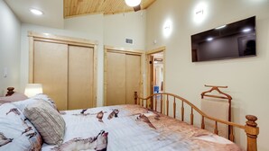 Une chambre à coucher avec un lit, un plafond en bois et un téléviseur fixé au mur.