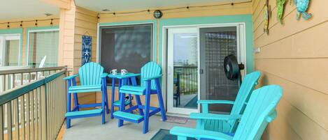 A balcony with blue Adirondack chairs, a small table, and a door leading to an outdoor area.