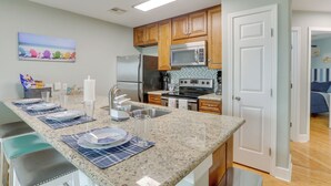 A kitchen with granite countertops, wooden cabinets, stainless steel appliances, and a breakfast bar with seating. - Walk to Seawall & Beach! Galveston Condo w/ Pool (Galveston)