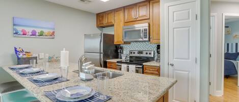 A kitchen with granite countertops, wooden cabinets, stainless steel appliances, and a breakfast bar with seating.
