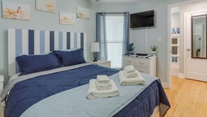 A bedroom with a bed, a bedside table, a TV, and a window with curtains. - Walk to Seawall & Beach! Galveston Condo w/ Pool (Galveston)
