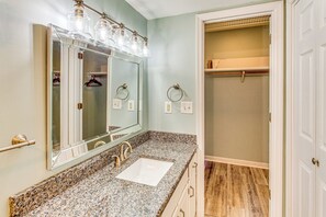 Une salle de bain dotée d’un comptoir en granit, d’un lavabo, d’un grand miroir et d’un dressing avec un plancher en bois.