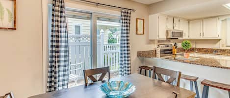 A dining area with a table, chairs, and a blue glass bowl. There is a kitchen area with cabinets and a microwave.