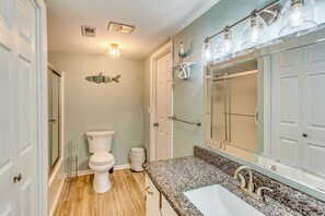 Une salle de bain avec des toilettes blanches, un lavabo doté d’un plan de travail en granit et un grand miroir.