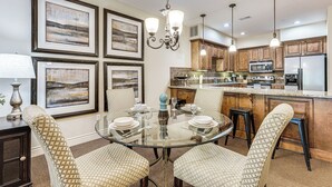 A dining area with a glass table, cushioned chairs, framed artwork on the walls, and wooden cabinets in the background. - Quiet Condo w/ Patio: 3 Mi to Dtwn Branson! (Branson)