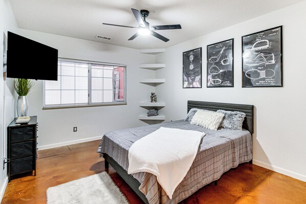 A bedroom with a bed, a ceiling fan, a window, and wall art.