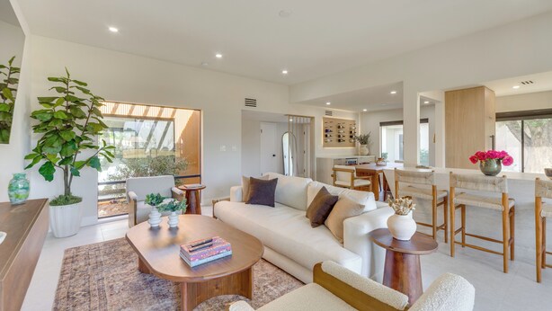 A spacious living area with a sofa, coffee table, and chairs. There is a dining area with a table and chairs. A large plant is visible in the corner. - Rancho Mirage Condo Near El Paseo & The River! (Rancho Mirage)