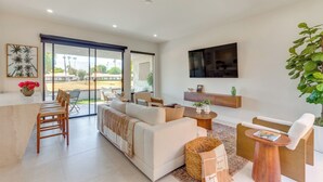 A modern living room with a sofa, chairs, a TV, and a large window. - Rancho Mirage Condo Near El Paseo & The River! (Rancho Mirage)