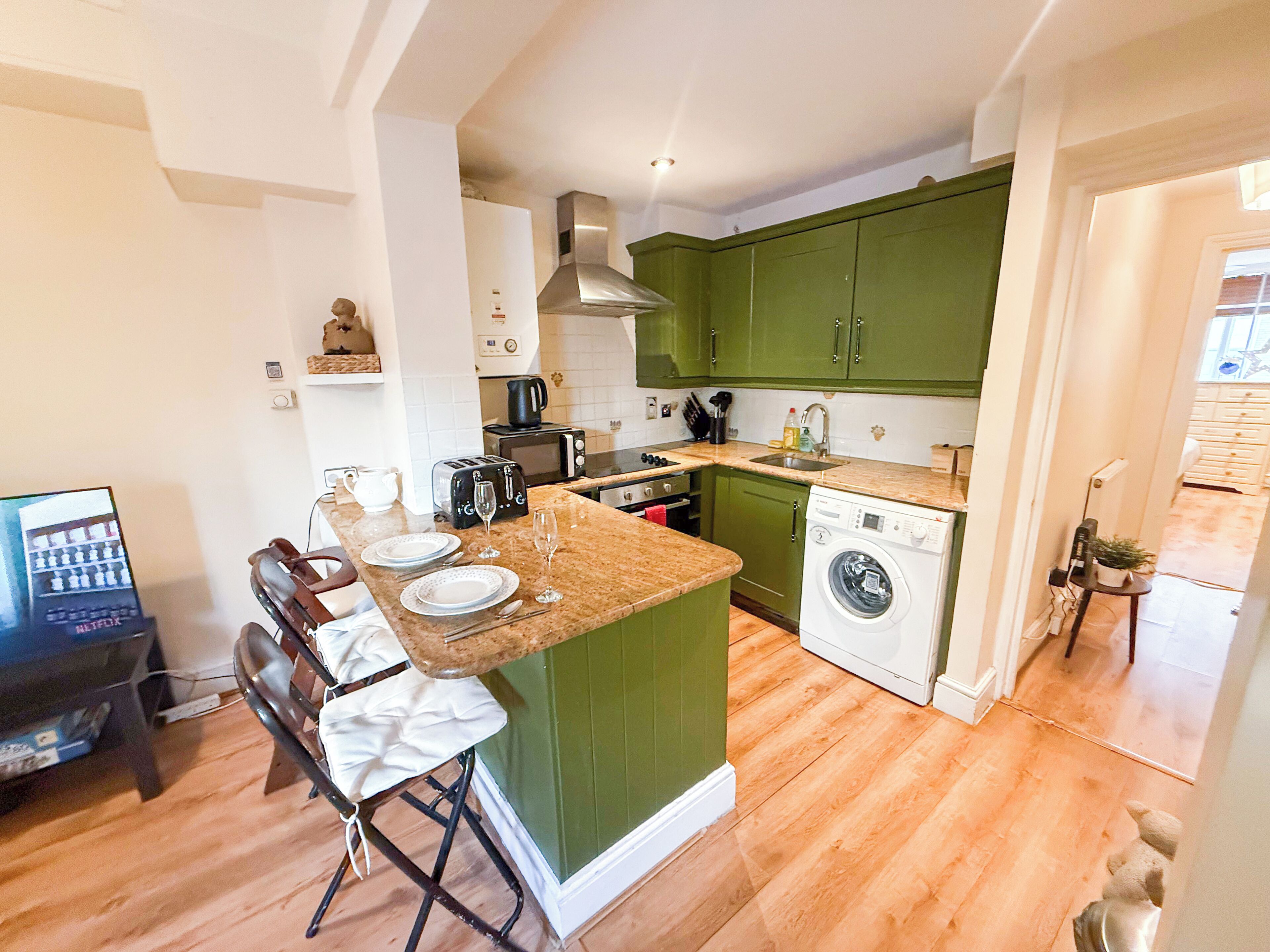 A compact kitchen with a central island, a washing machine, and a dining area with chairs.