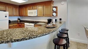 Una cocina con gabinetes de madera, microondas, estufa, encimeras de granito y taburetes de bar.