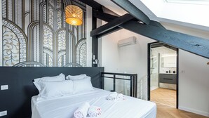 A modern bedroom with a bed, a skylight, a patterned wall, and a view to a bathroom. - Matterhorn (Annecy)