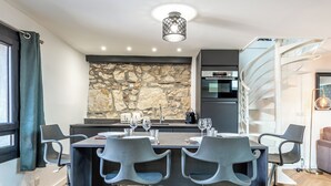 A modern kitchen with a stone backsplash, a dining area with four chairs, and a spiral staircase. - Matterhorn (Annecy)
