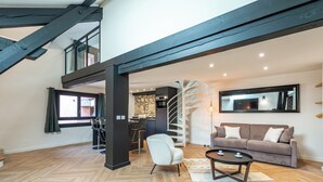 A spacious loft with a herringbone wood floor, a modern kitchen, a dining area with bar stools, a living room with a sofa and coffee table, and a spiral staircase. - Matterhorn (Annecy)