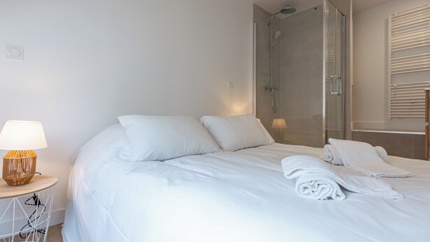 Une chambre moderne avec un grand lit, une table de chevet avec une lampe et une douche séparée par une paroi en verre.