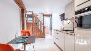 Une cuisine moderne avec un escalier en bois, un coin repas avec des chaises orange et une vue sur l’extérieur.