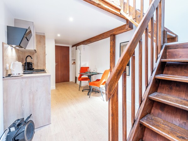 A compact kitchen with modern appliances, a dining area with a table and chairs, and a wooden staircase.