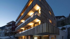 A modern multi-story building with a wooden facade and illuminated balconies. - Alpine Myth (Sankt Anton am Arlberg)