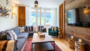 A modern living room with a sofa, a coffee table, a TV, and a view of a green landscape. - Alpine Myth (Sankt Anton am Arlberg)