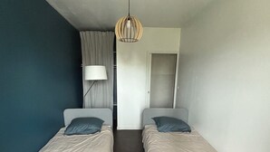 Una habitación con dos camas individuales, una lámpara en el techo, una puerta y una ventana con cortinas.