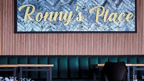 A restaurant interior with a sign reading "Ronny's Place" above a counter with glasses and napkins. - Ronny's Flat Manuel Antonio (Quepos)