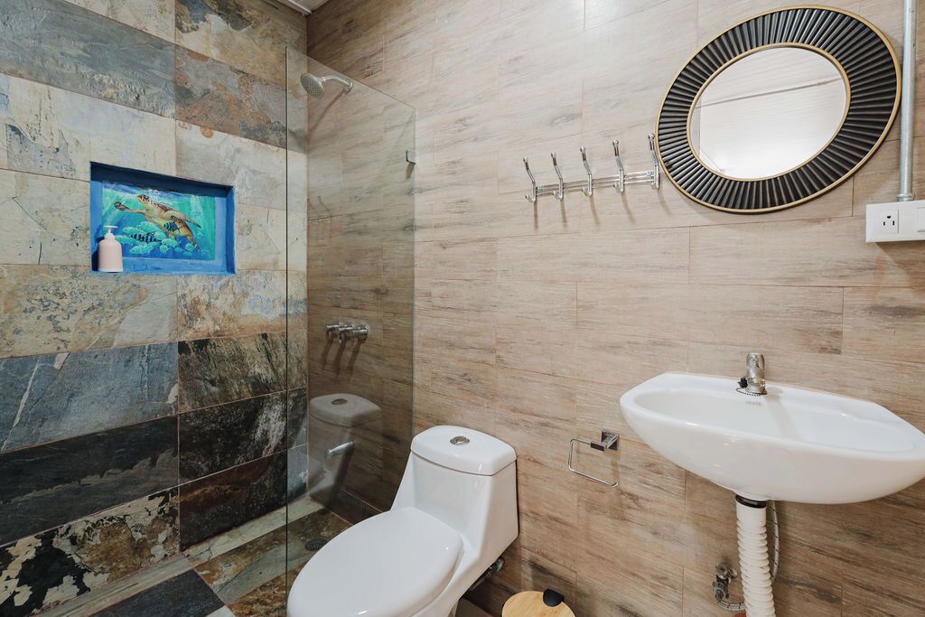 A bathroom with a toilet, sink, and shower. There is a framed picture on the wall and a mirror above the sink.