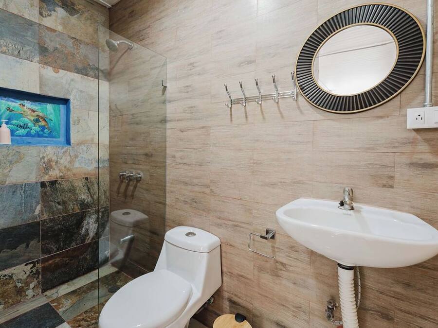 A bathroom with a toilet, sink, and shower. There is a framed picture on the wall and a mirror above the sink.