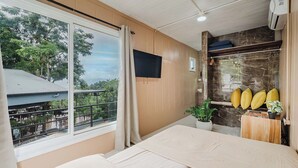 A hotel room with a large bed, a television mounted on the wall, a window with a view of the outdoors, and a small plant on a wooden side table. - Ronny's Flat Manuel Antonio (Quepos)
