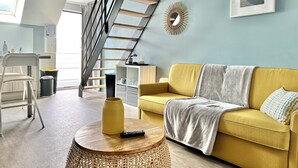 A modern living room with a yellow sofa, a round wooden table, a staircase, and a framed picture on the wall. - Le Patio de Loiseau  (Le Mans)