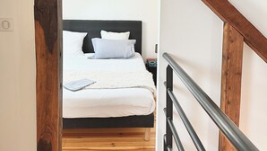 A bedroom with a bed, white bedding, a wooden headboard, and a staircase with a metal railing. - Le Patio de Loiseau  (Le Mans)