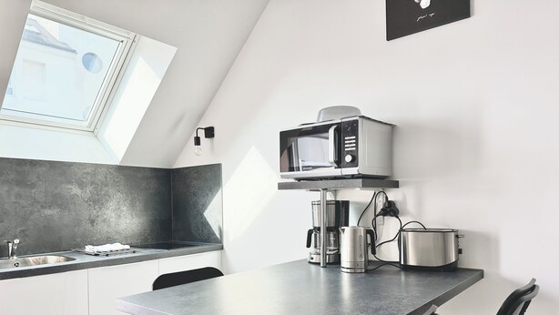 A modern kitchen with a built-in microwave, coffee maker, and kettle on the countertop. - Le Patio de Loiseau  (Le Mans)