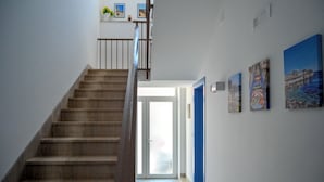 Eine Treppe führt zu einer Tür mit blauem Rahmen, begleitet von Wänden mit gerahmten Kunstwerken.