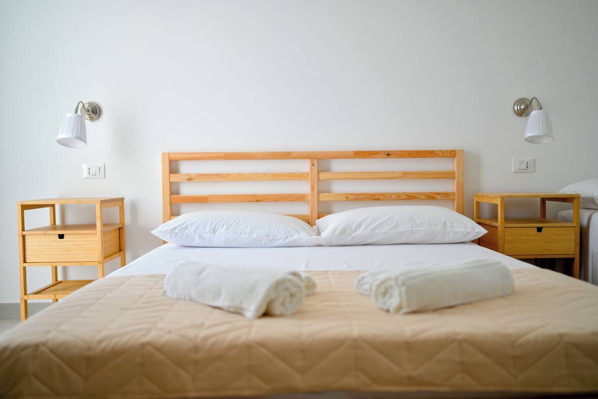 Un lit bien fait, avec une tête de lit en bois, deux tables de chevet avec des lampes et un mur blanc.