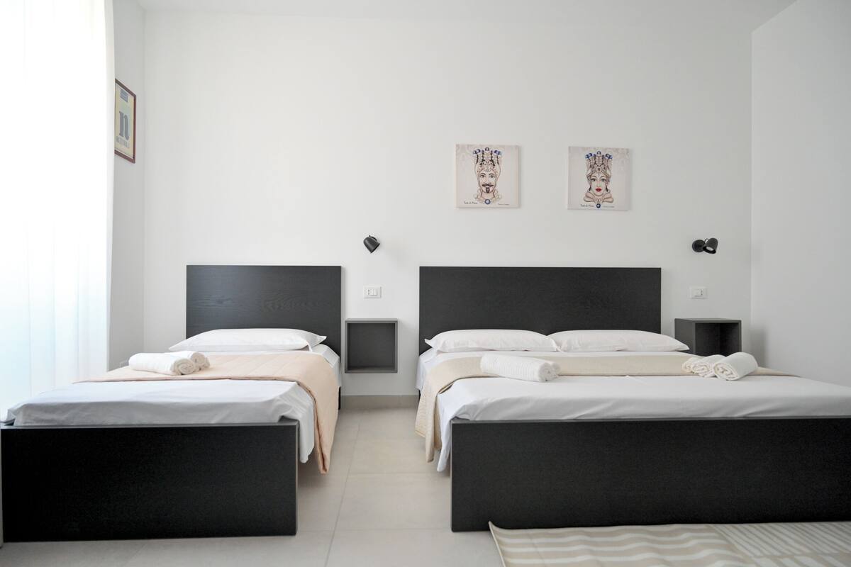 Une chambre d’hôtel avec deux lits, chacun doté d’une tête de lit noire, de draps blancs et d’une petite table de chevet avec une lampe. Deux œuvres d’art encadrées sont accrochées au mur au-dessus des lits.