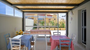 Eine Terrasse im Freien mit Holzboden, weißen Stühlen und Tischen, die mit karierten Tischdecken bedeckt sind.