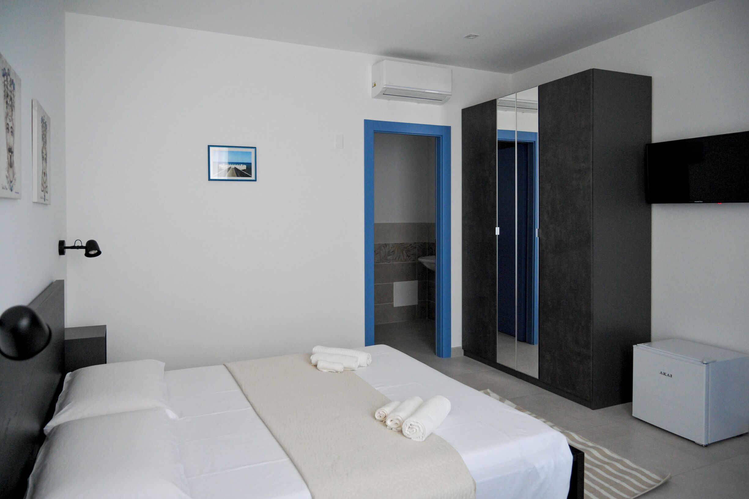 Una habitación de hotel moderna con una cama grande, un televisor de pantalla plana y un baño visible a través de una puerta abierta.