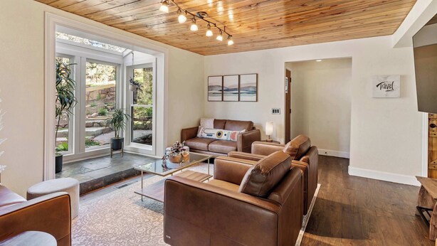 Una sala de estar moderna con techo de madera, sofás de cuero, una mesa de centro de vidrio y vistas a un área exterior a través de puertas de cristal.
