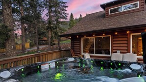 Un jacuzzi con muelle de madera, pared de piedra y vistas al bosque circundante.